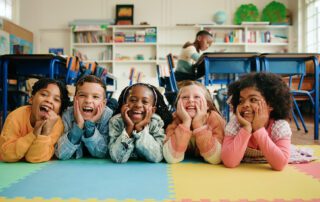 children smiling while they lie on their stomach with their heads in their hands having fun in a classroom